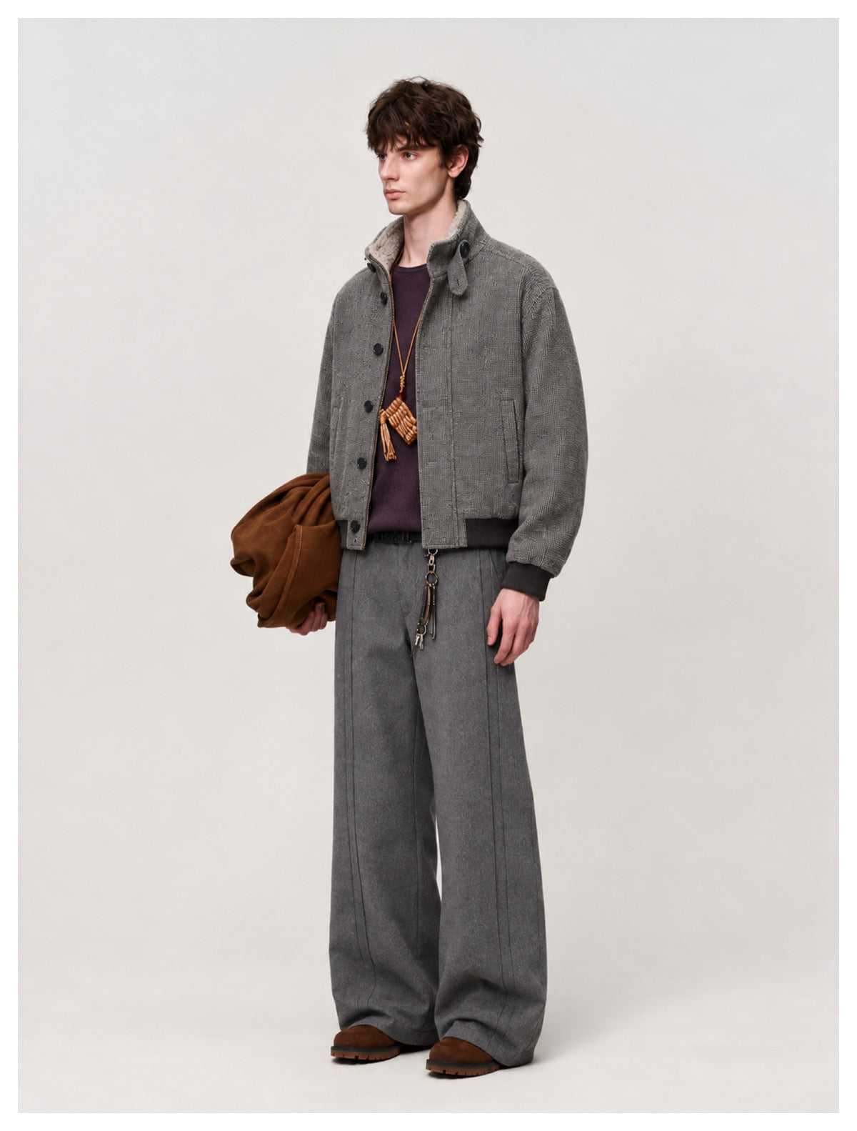Model wearing gray wide-leg pleated trousers with a gray bomber jacket, purple top and brown shoes