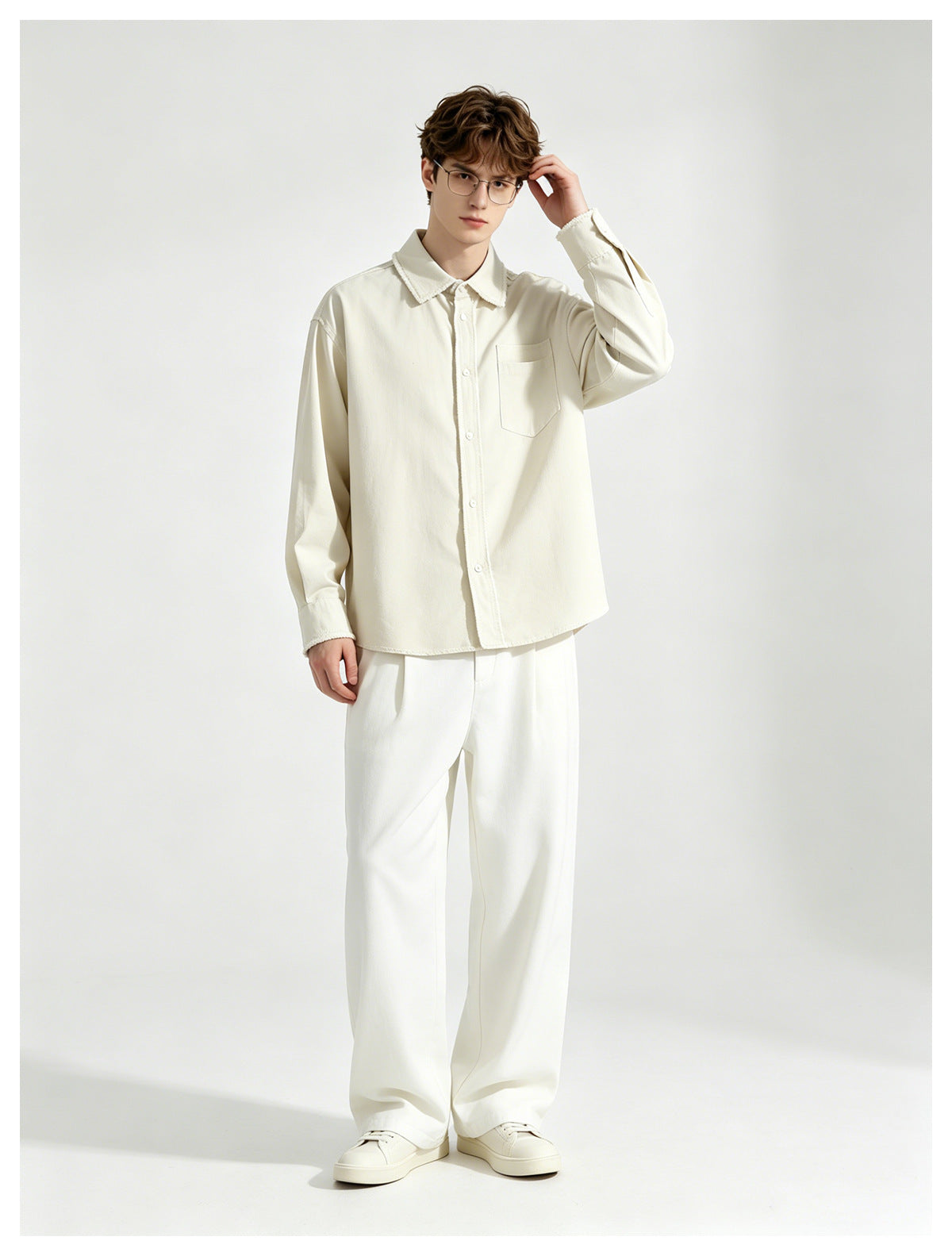 Model wearing a beige frayed-edge button-up shirt with white wide-leg trousers and white sneakers, hand raised to head