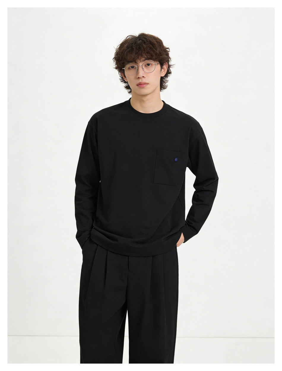 Model wearing a black long-sleeve crewneck shirt with a chest pocket and black trousers.