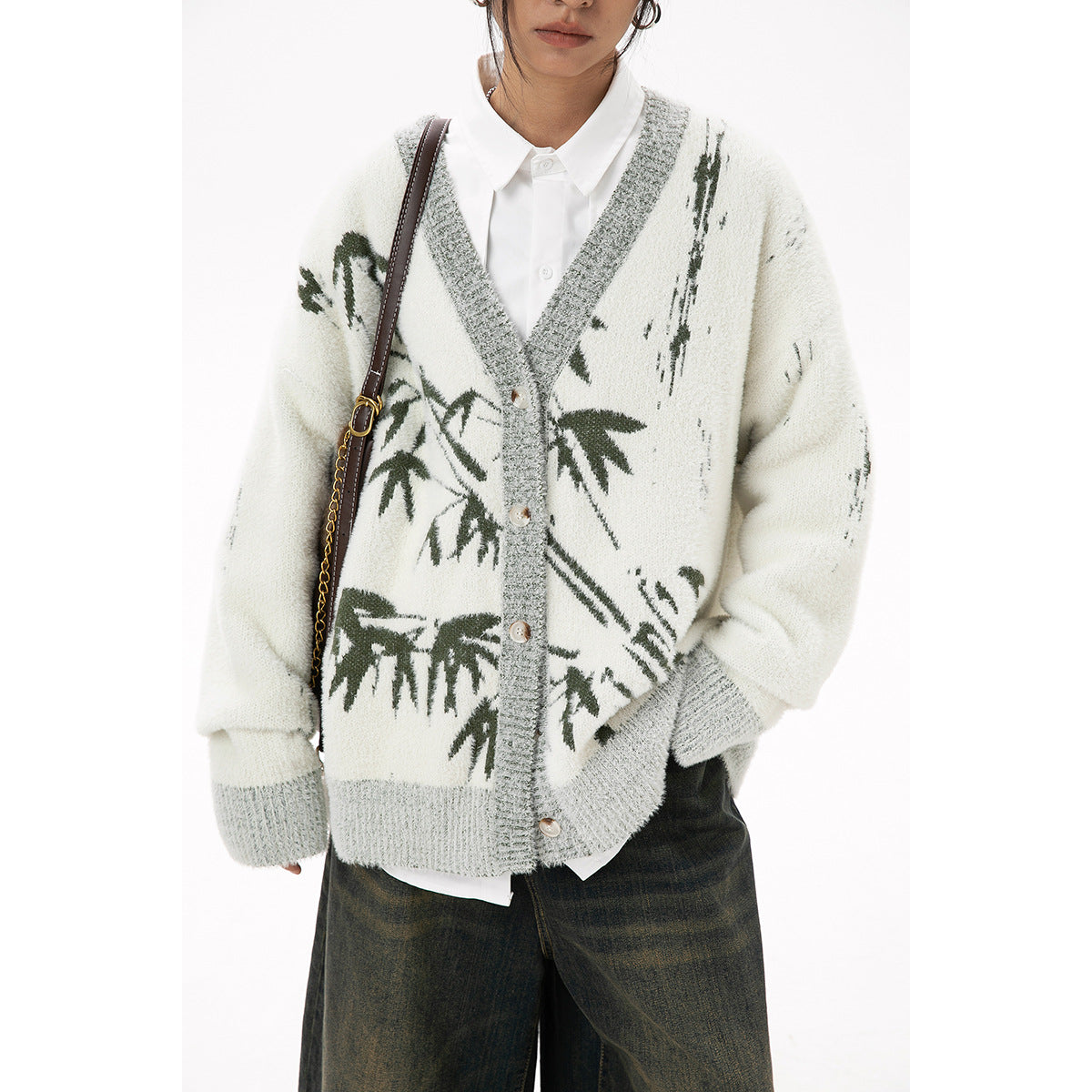 Close view of an ivory cardigan with gray trim, buttons, and dark green botanical motifs worn over a white shirt.