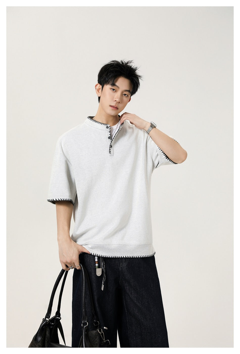 Model wearing a light gray short-sleeve henley with black contrast stitching and dark wide-leg jeans.