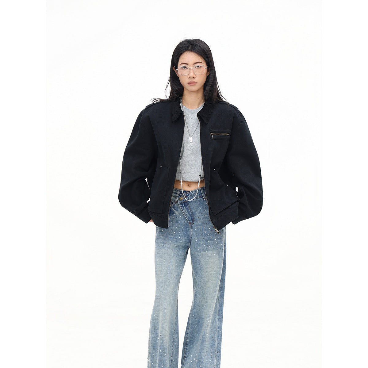 Front view of a model in an open black oversized jacket with a zip chest pocket, gray crop top, and embellished jeans.