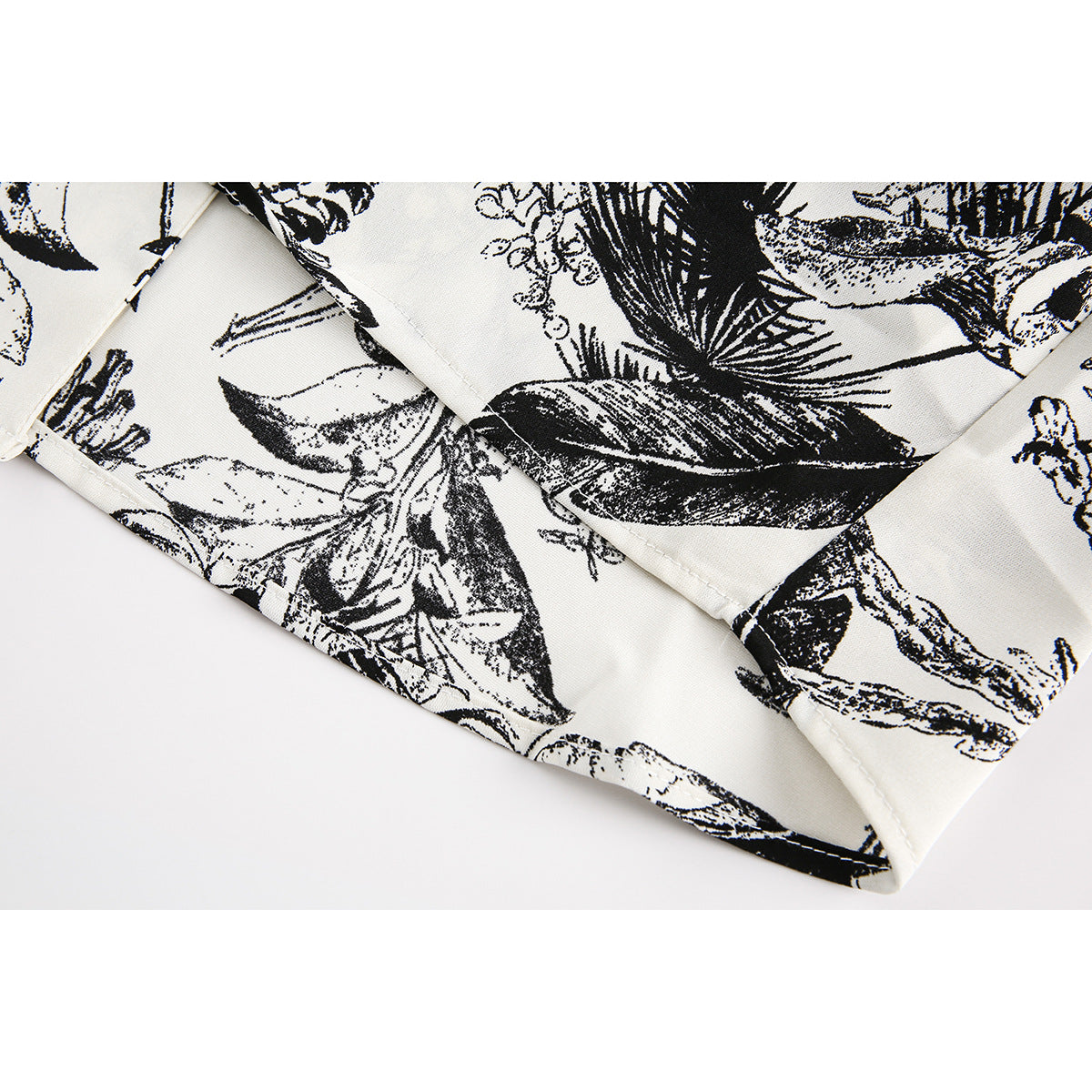 Close-up of the ivory garment's black botanical print and stitched hem.