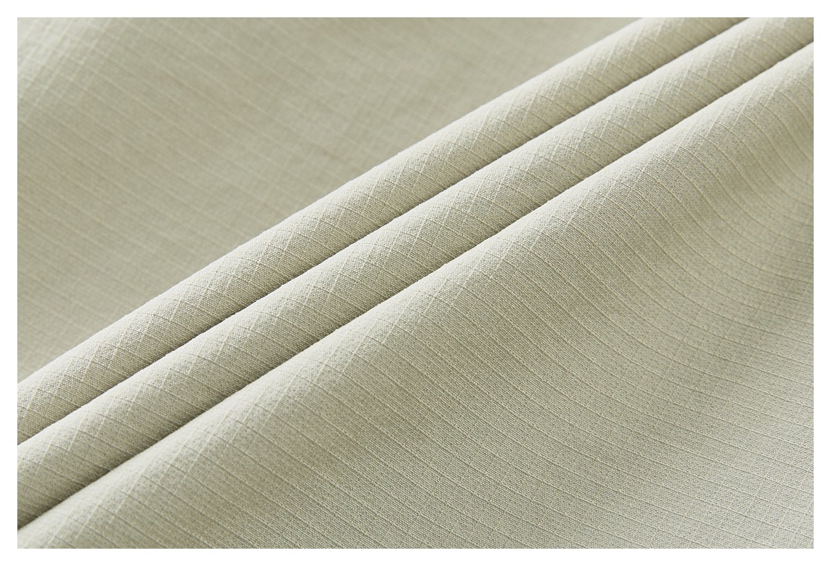Close-up of pale beige woven fabric folded into several diagonal ridges, showing its fine textured surface.