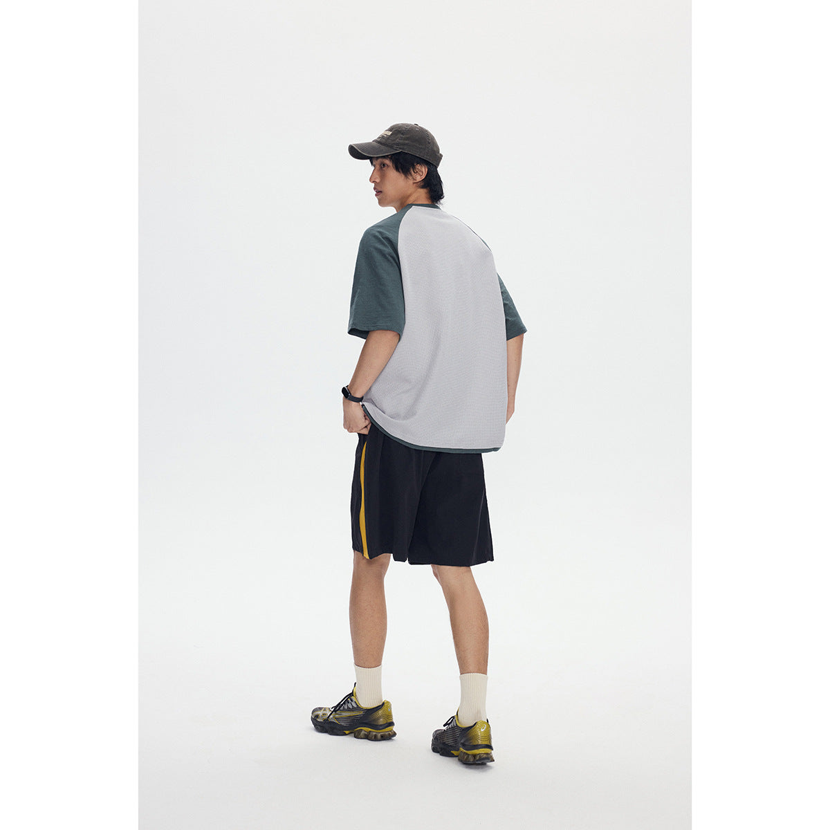 Rear view of a model wearing a light gray henley with dark green raglan sleeves and black shorts with a yellow side stripe.