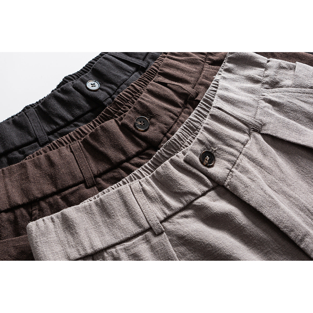 Close-up of black, brown, and light gray shorts showing gathered waistbands, buttons, and belt loops.