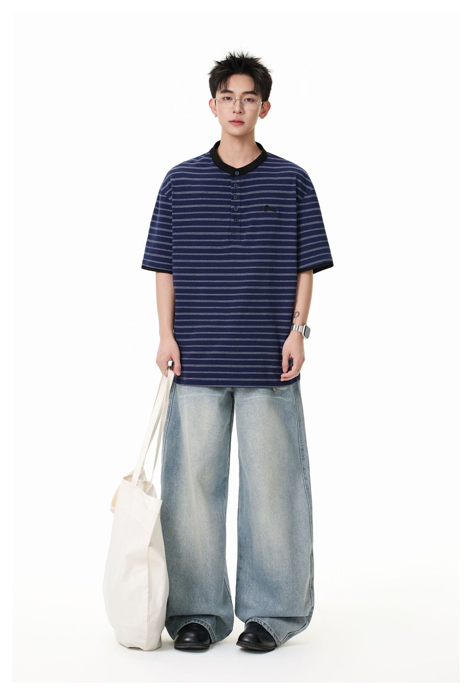 Model wearing the navy striped Henley T-shirt with wide-leg light-wash jeans and holding a white tote bag