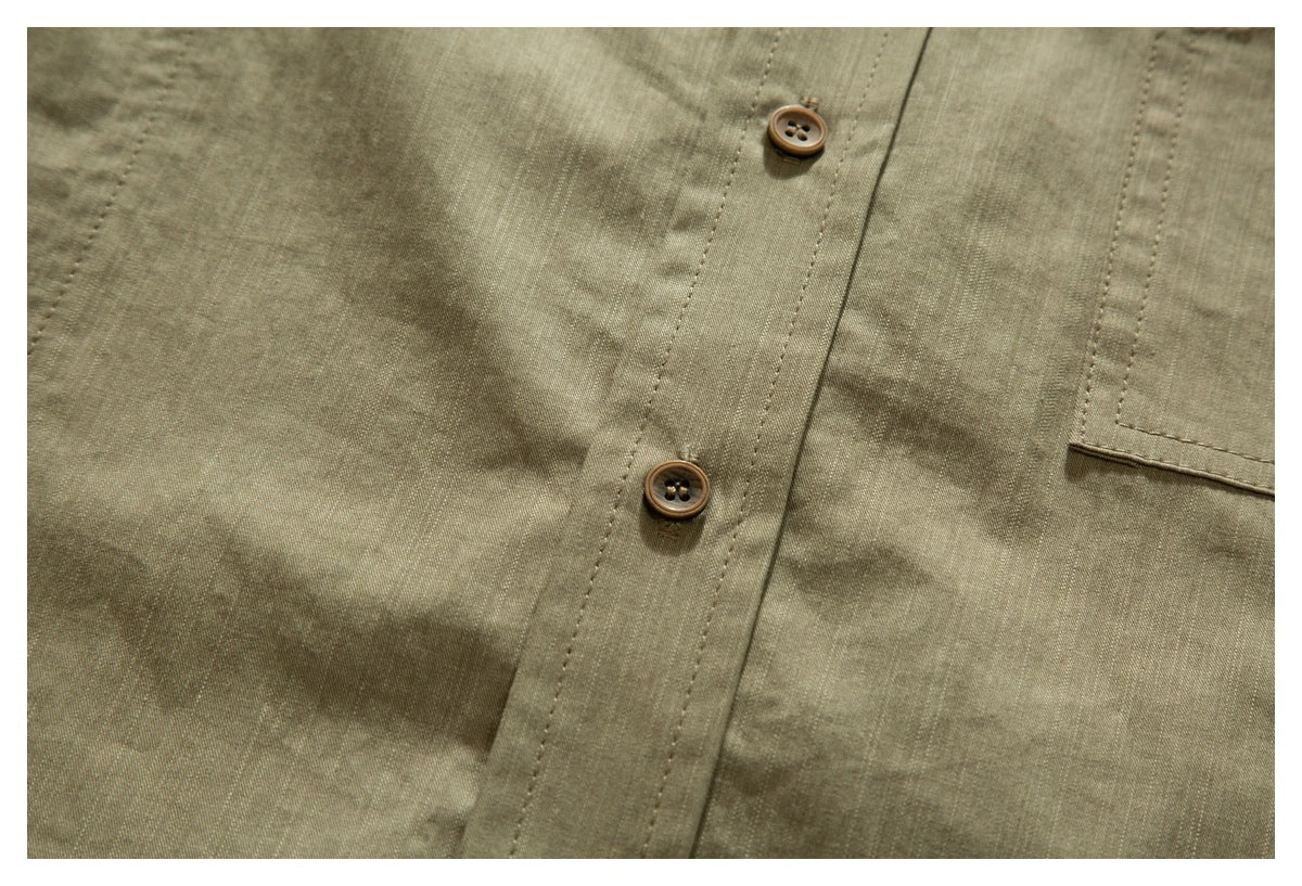 Close-up of an olive-khaki shirt front with brown buttons, stitched placket, and edge of a chest pocket.