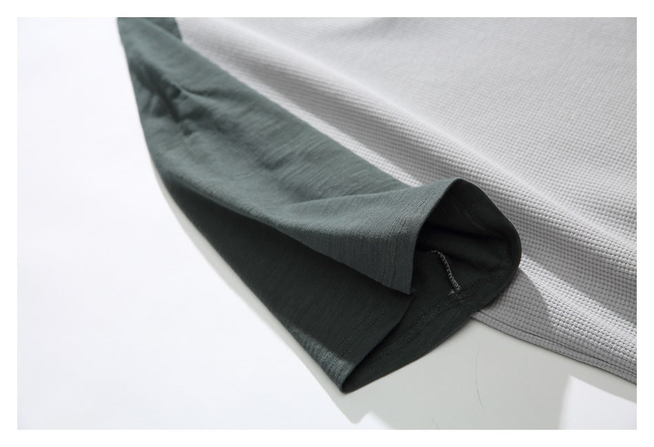 Close-up of the dark green sleeve and stitching on a light gray waffle-knit shirt.