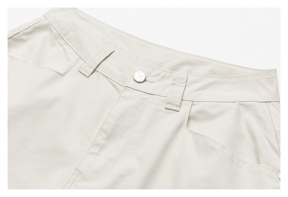 Close-up of ivory trousers showing the front waistband, button, belt loops and pocket openings.