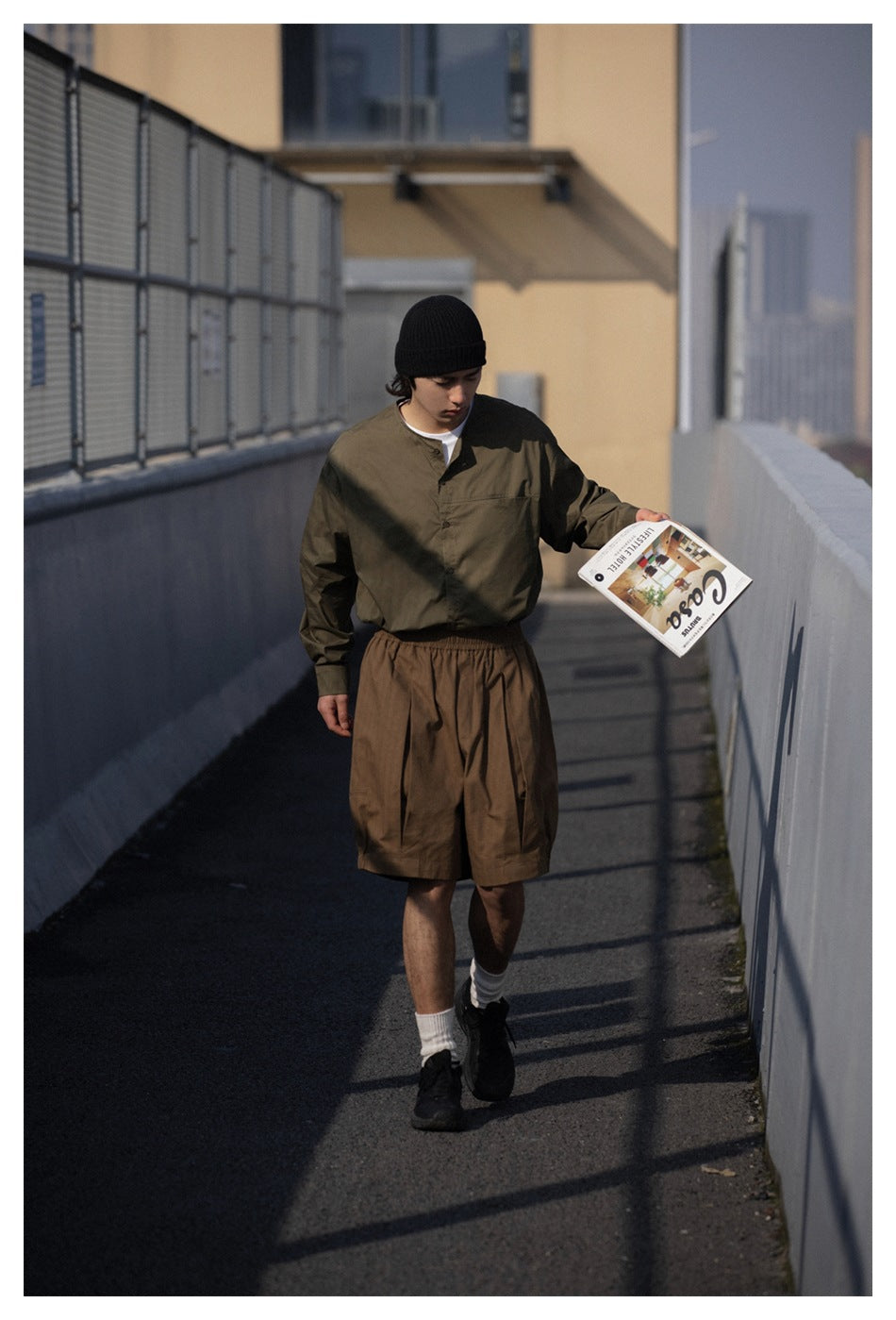 Model wearing an olive button-front shirt and loose brown shorts with elastic cuffs, outdoors.