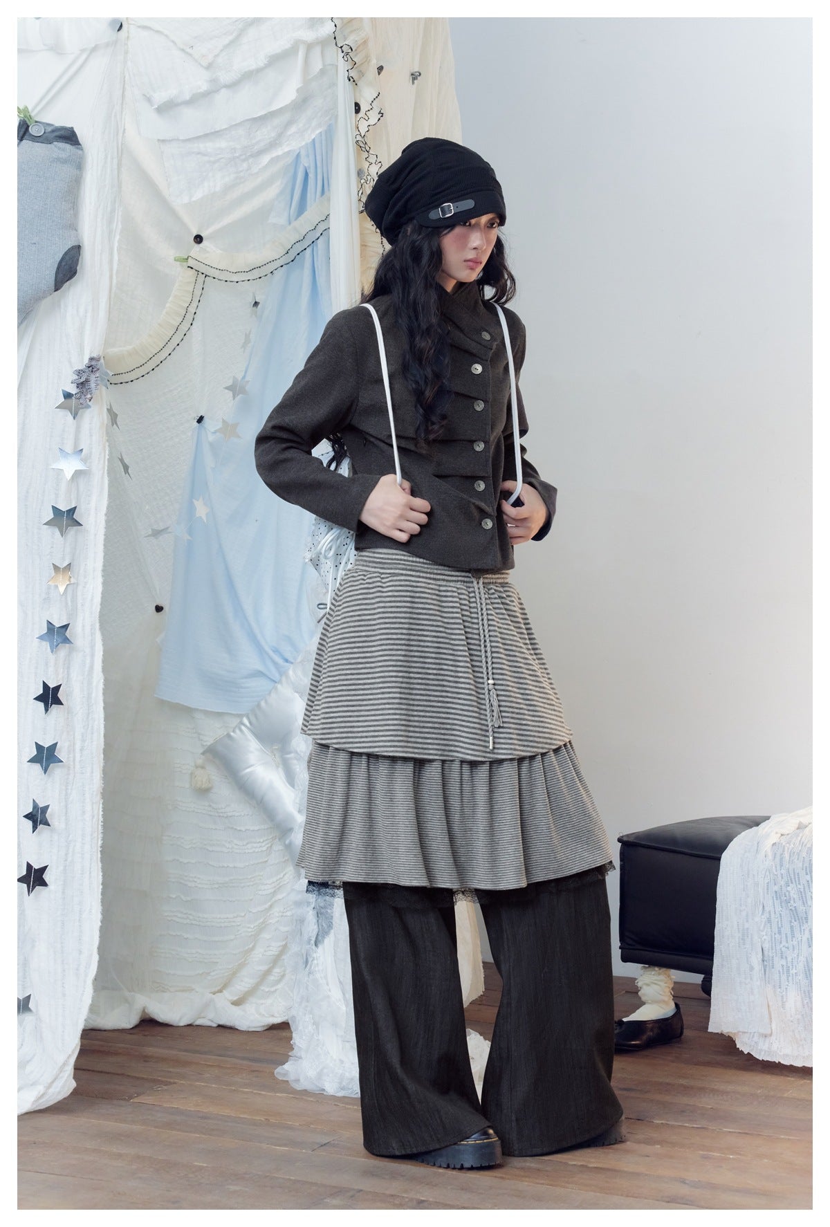 Model in a gray striped tiered skirt-over-pants with wide dark legs, styled with a gray jacket and black beanie