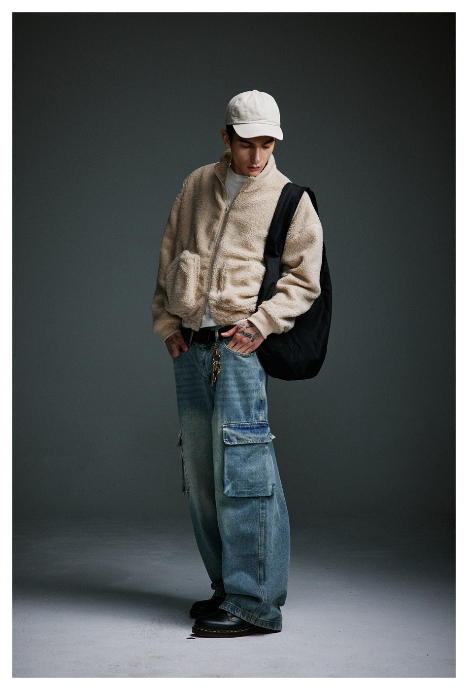 Model in a cream zip-up jacket and oversized blue cargo jeans, shown at an angle with a black shoulder bag.