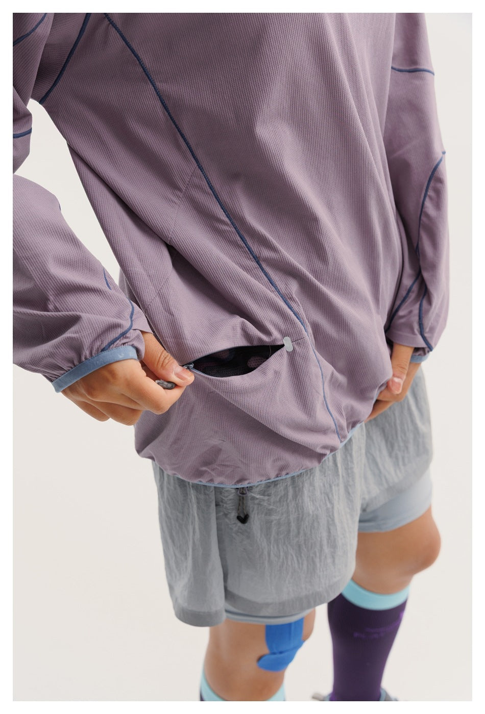 Close-up of the lavender top showing blue seam piping and a small zippered side pocket near the hem.
