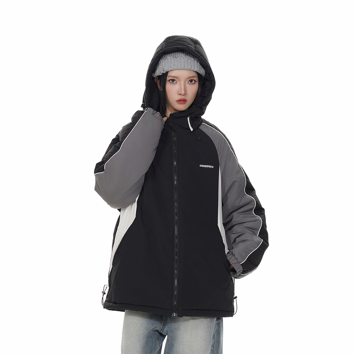 Closer front view of a model in a zipped black hooded jacket with gray and white panels and white piping.