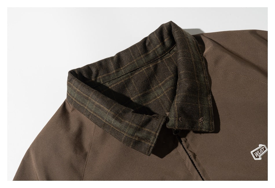 Close-up of a brown jacket with its plaid-lined collar turned up and an embroidered chest emblem.