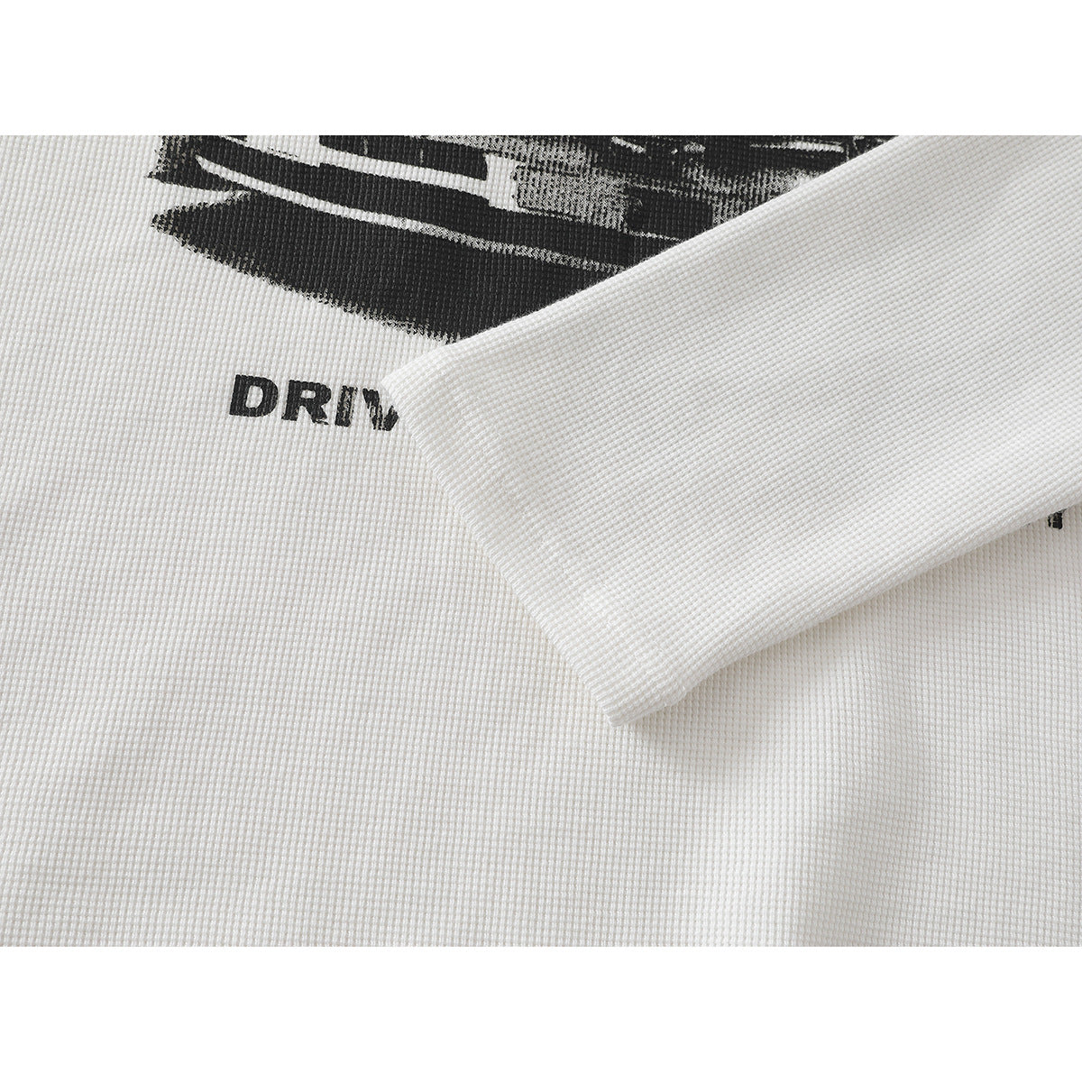 Close-up of a white textured shirt with a folded sleeve partly covering a black graphic and partial lettering.