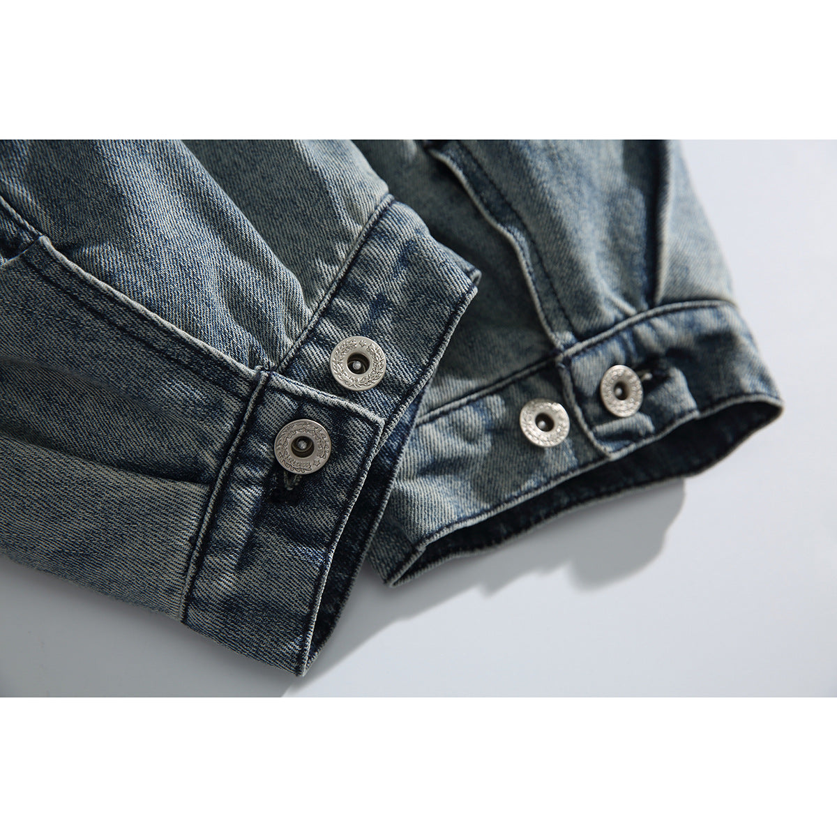 Close-up of blue denim jacket cuffs with silver snap buttons and faded, distressed detailing.