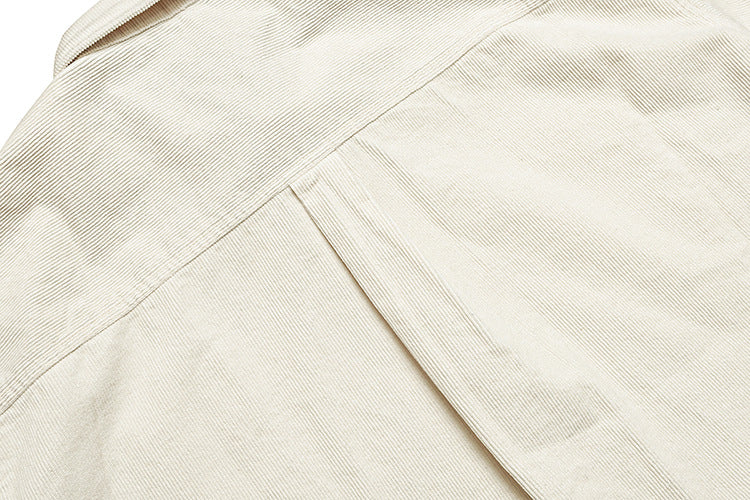 Close-up of cream ribbed shirt fabric with intersecting seams and a folded edge.