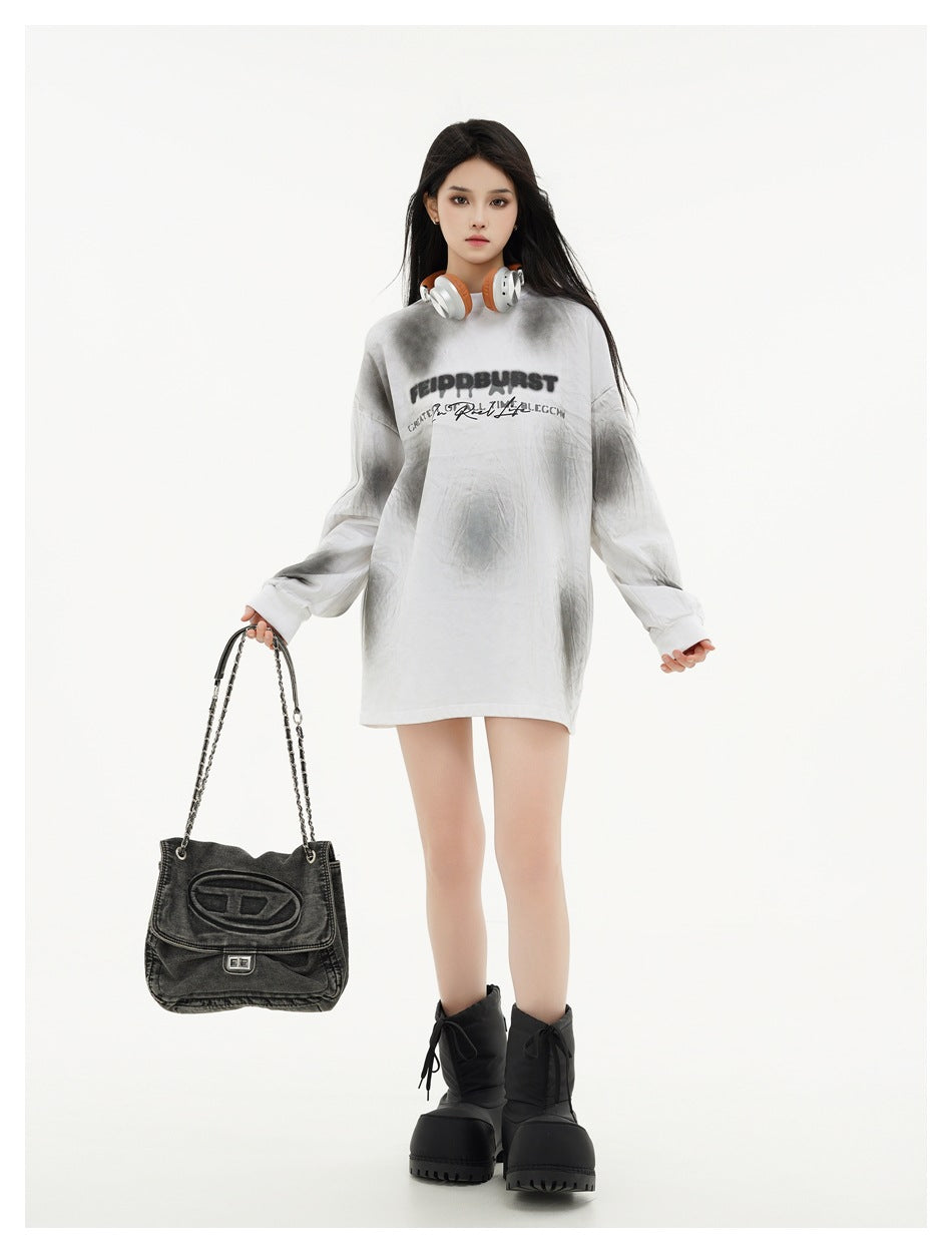 Model wearing an oversized white and gray tie-dye shirt with black chest lettering, holding a black handbag.