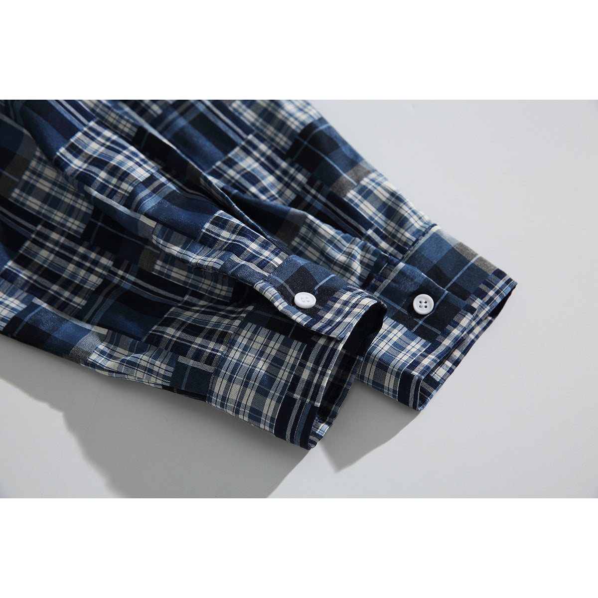 Close-up of the plaid shirt's sleeve cuffs and white buttons on a light background.