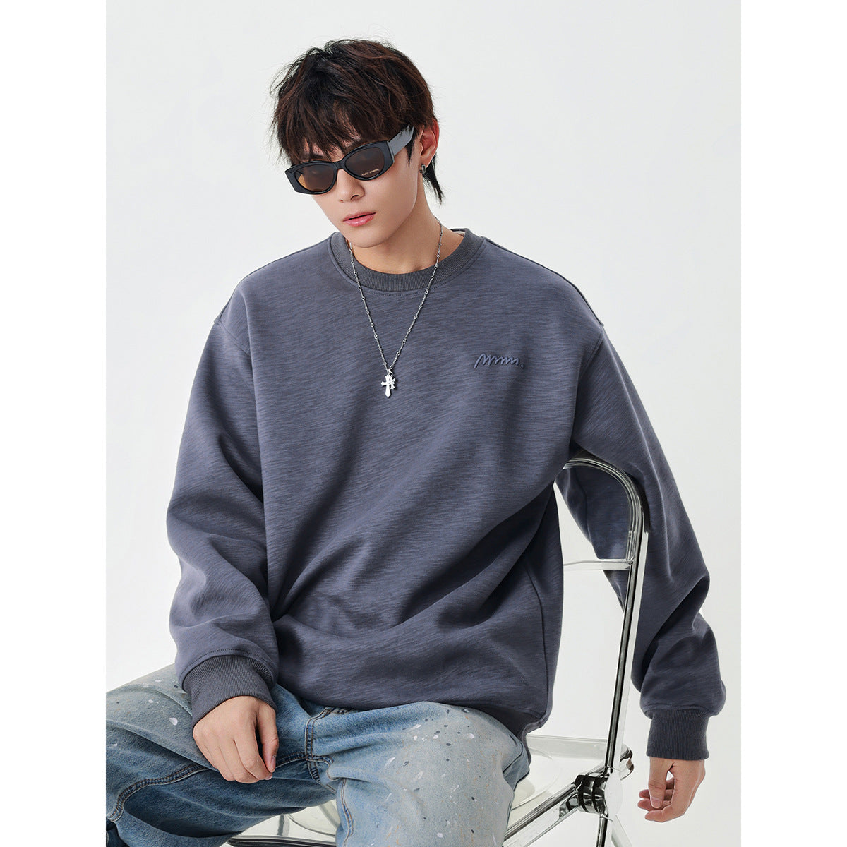 Model wearing an oversized slate-gray crewneck sweatshirt with ribbed cuffs and a small embroidered chest logo.