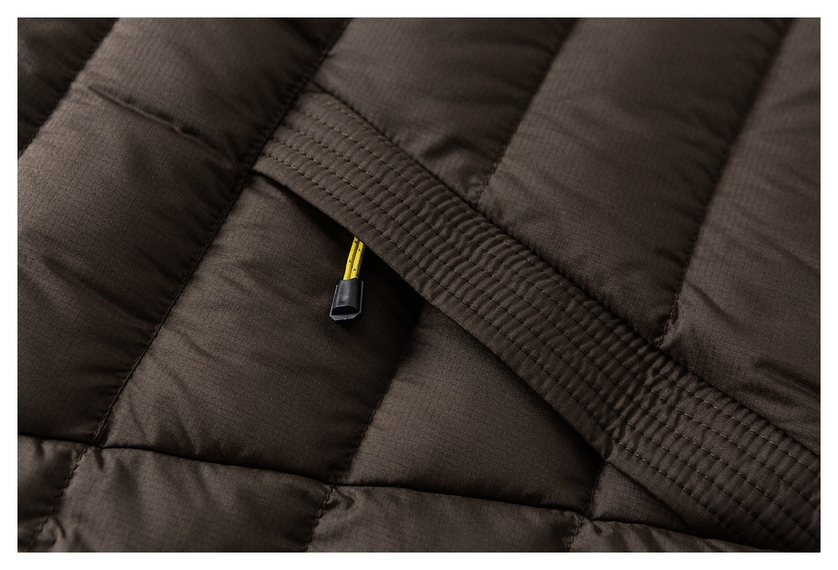 Close-up of brown quilted jacket stitching with a yellow cord and black tip beneath a stitched flap.