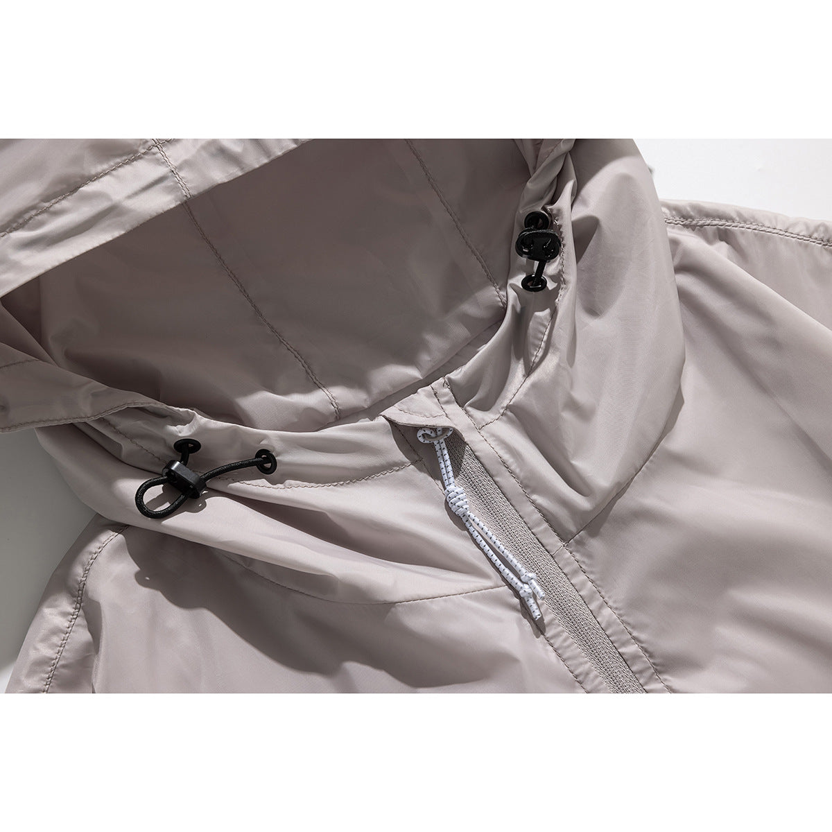 Close-up of a light taupe hooded jacket showing adjustable hood cords, black toggles and a front zipper.