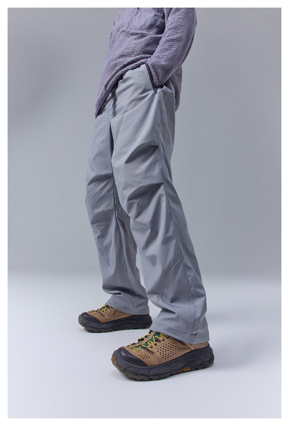 Side view of a person wearing loose gray pants with a zippered pocket and curved leg seams.