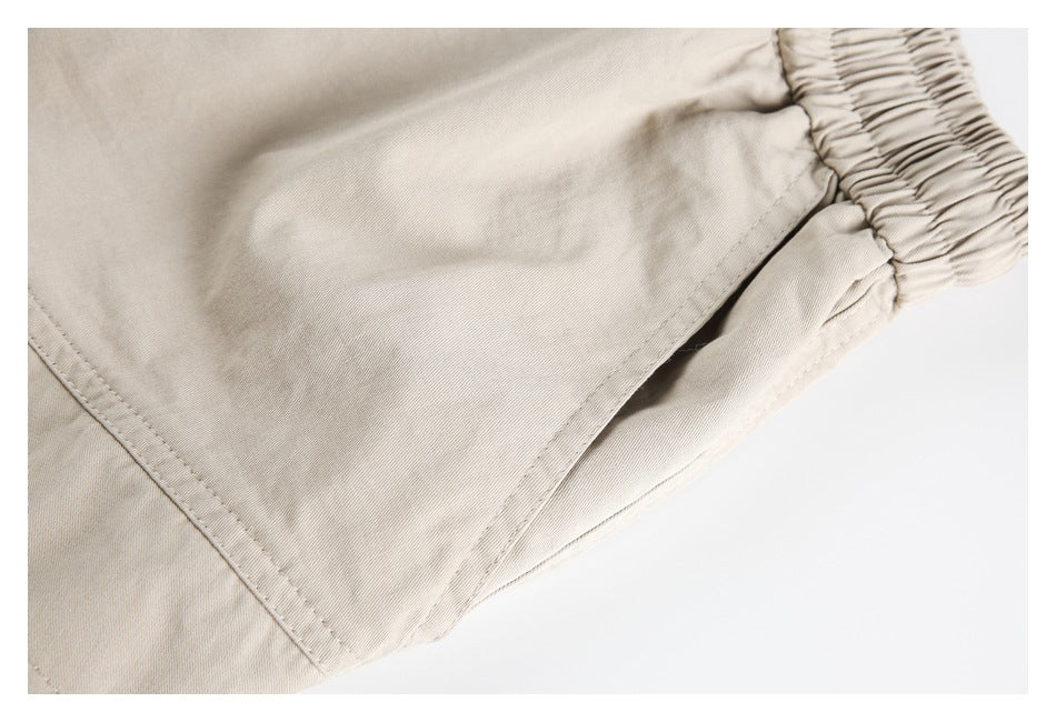 Close-up of a beige pant leg with a gathered elastic ankle cuff and stitched seam.