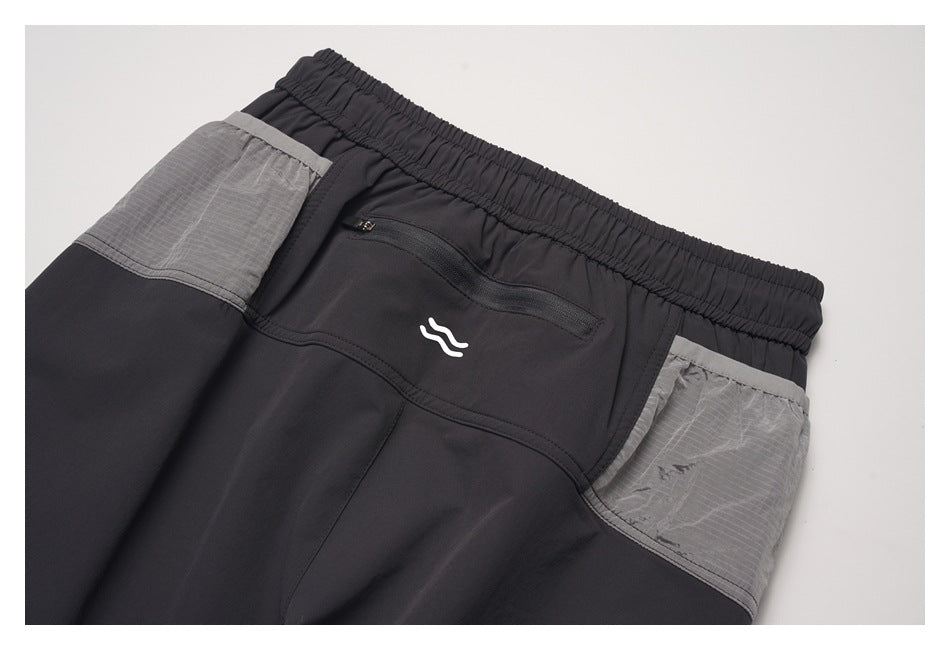 Close-up of black pants with an elastic waistband, zippered back pocket, white logo and gray side panels.