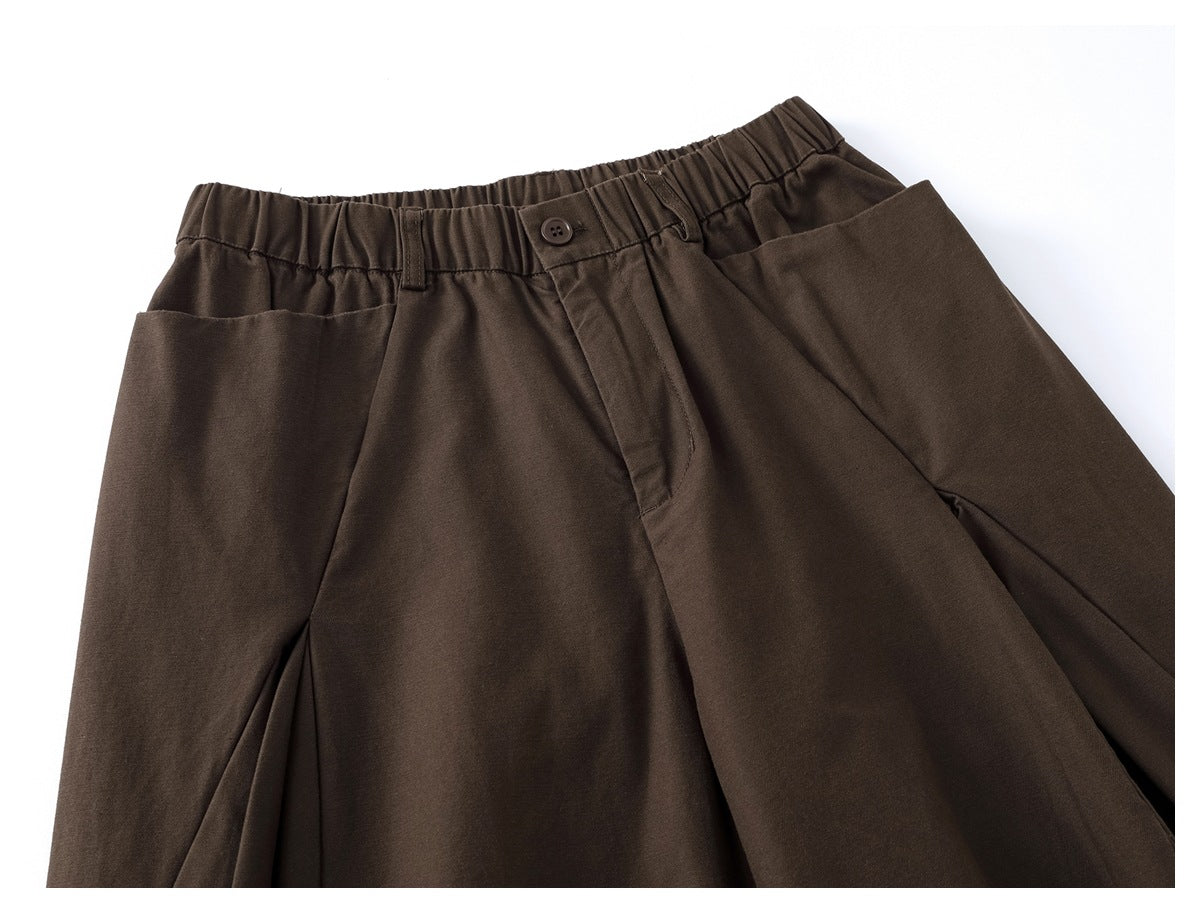Dark brown trousers shown from the front, with an elastic waistband, button closure, pleats and angled pockets.