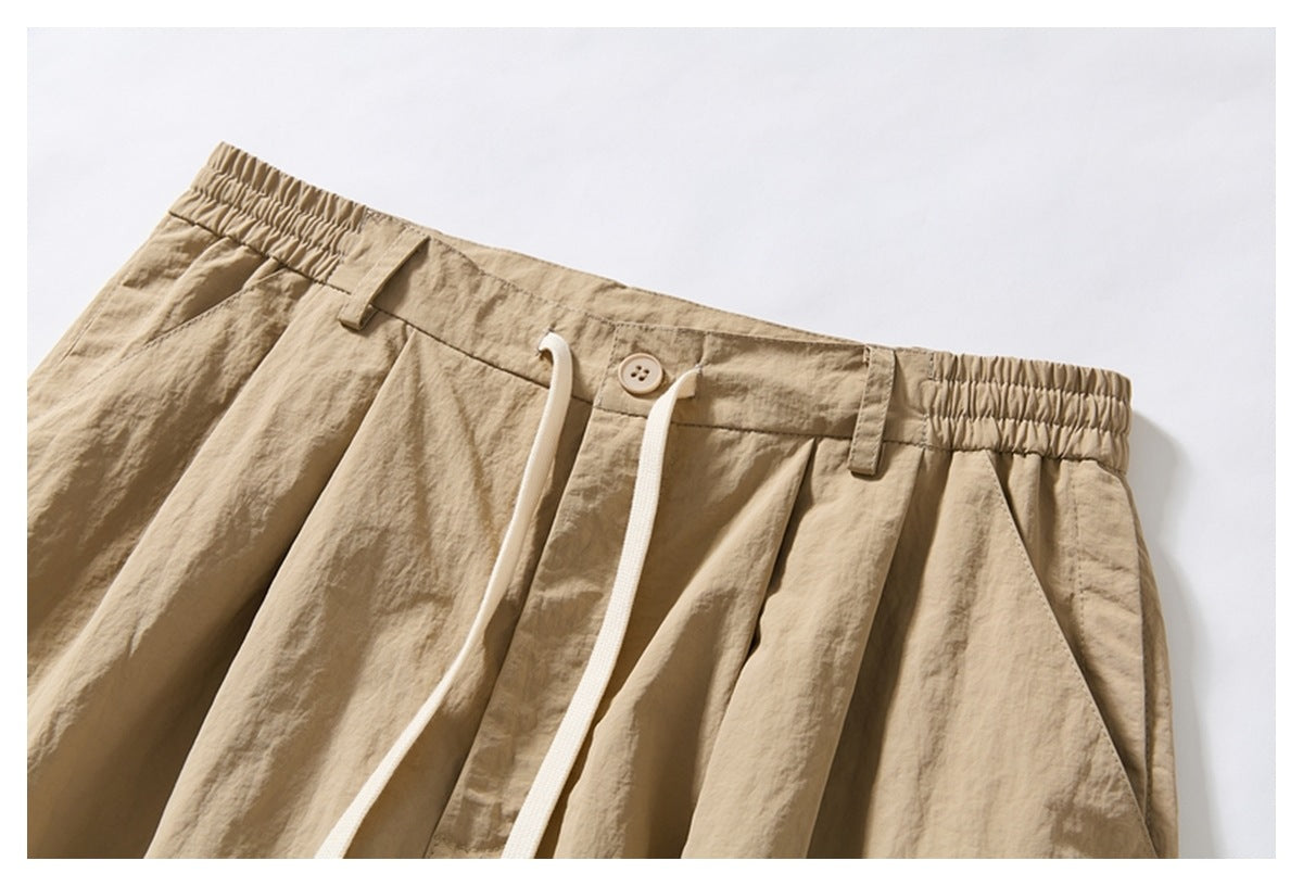 Close-up of beige wide-leg shorts showing the elasticated waistband, button, drawstring, pleats and side pocket.