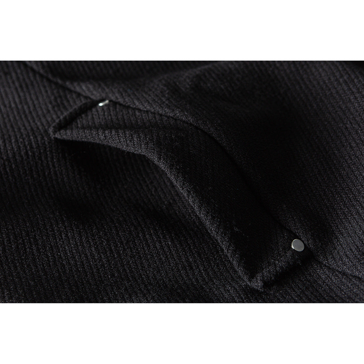 Close-up of black textured fabric and a flap pocket secured with a small metal snap.
