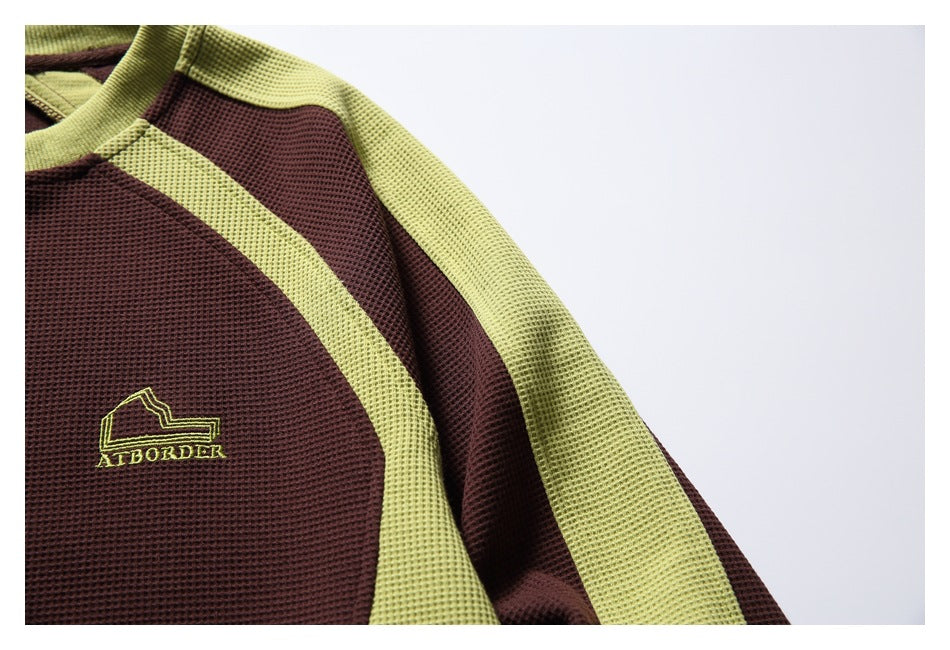 Close-up of a burgundy waffle-knit top with chartreuse color-blocking and a small embroidered chest logo.