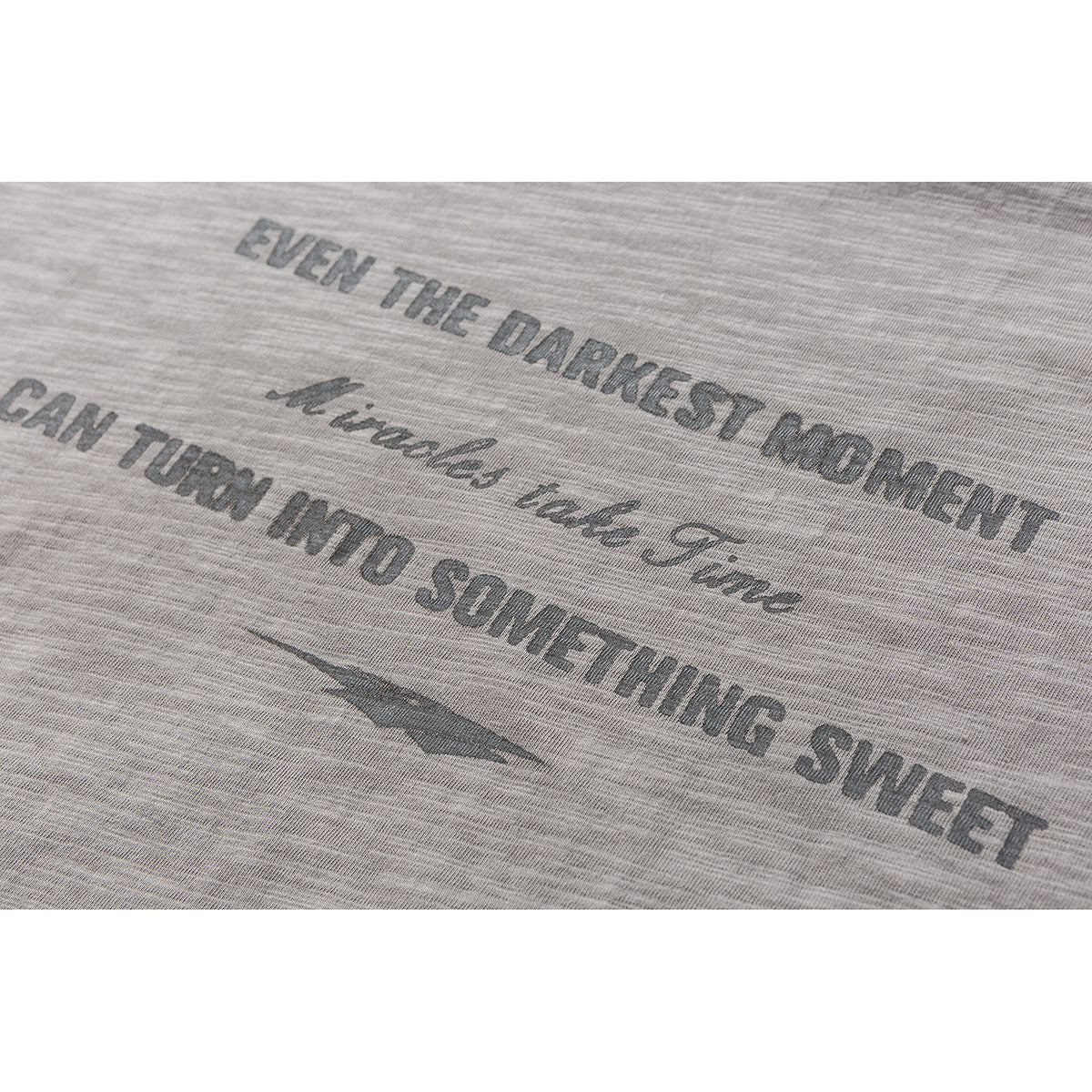 Close-up of dark English lettering and a small graphic printed on a gray marled T-shirt.