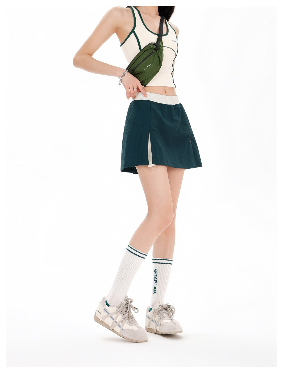 Model in a dark teal athletic skirt with a white waistband and side slit, shown at an angle with a cream top.