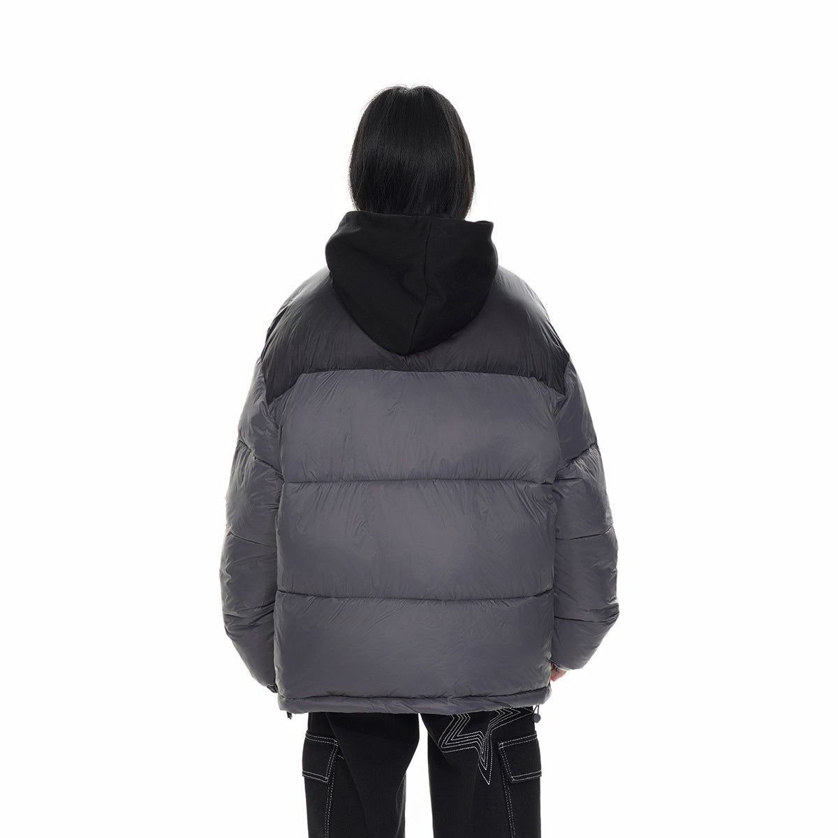 Back view of a model wearing a charcoal gray puffer jacket with a black hood and horizontal quilting.