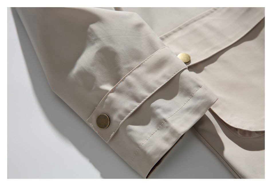 Close-up of a light beige jacket sleeve cuff with a brass-tone button and stitched tab.