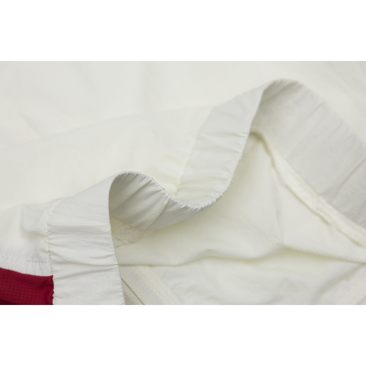 Close-up of ivory jacket fabric and curved stitched seams, with a small burgundy panel visible at the edge.