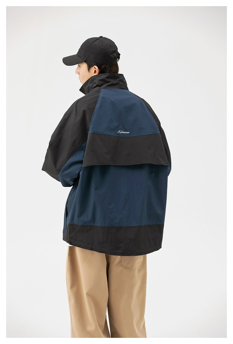 Model wearing a navy and black color-block jacket, shown from the back at an angle with tan trousers.