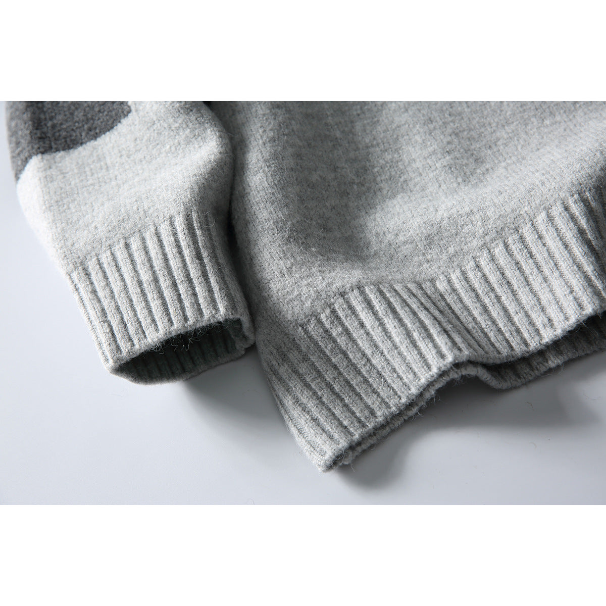 Close-up of a light gray sweater’s ribbed sleeve cuff and bottom hem, with a charcoal sleeve panel.