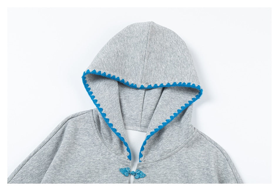 Close-up of a gray hoodie showing the hood's bright blue scalloped trim and decorative toggle closure.