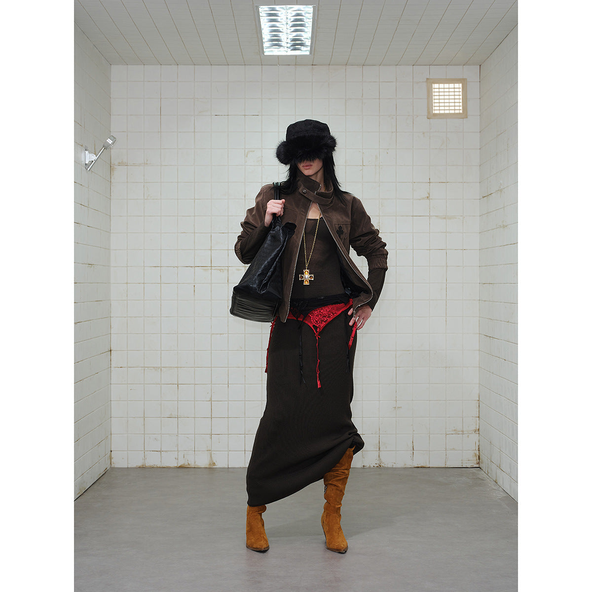 Model wearing a dark brown zip jacket with a long black skirt and red lace detail, posed in a tiled room.