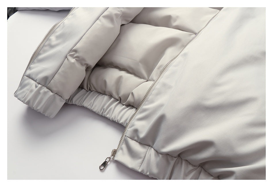 Close-up of a light gray padded jacket showing its open front zipper, quilted panels, and gathered hem.