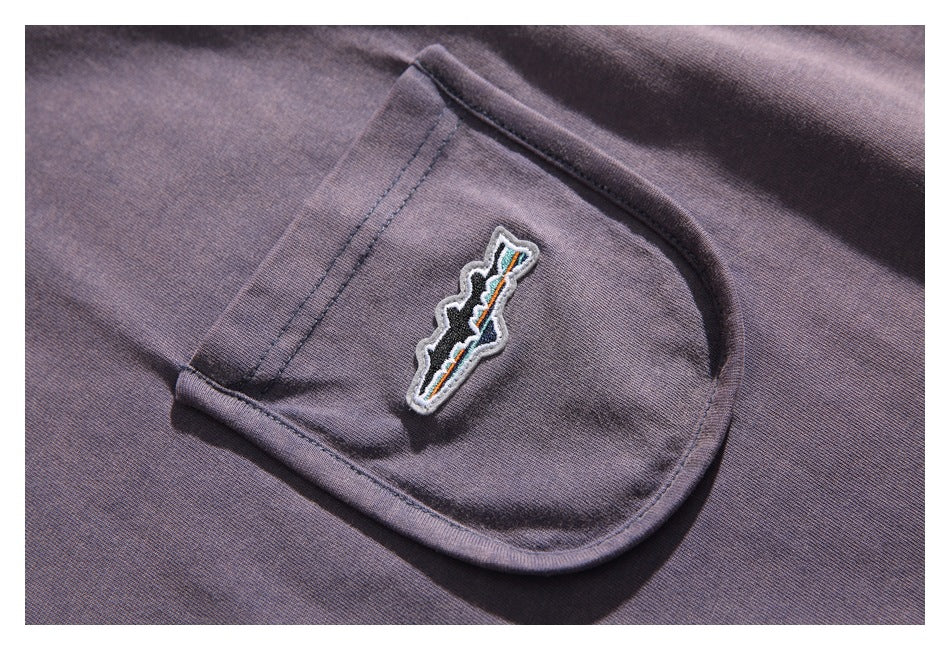 Close-up of the rounded chest pocket and embroidered patch on the purple-gray shirt.