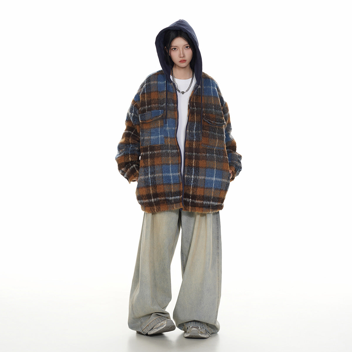 Model wearing a blue and brown plaid hooded jacket with a navy hood and light-wash wide-leg jeans.