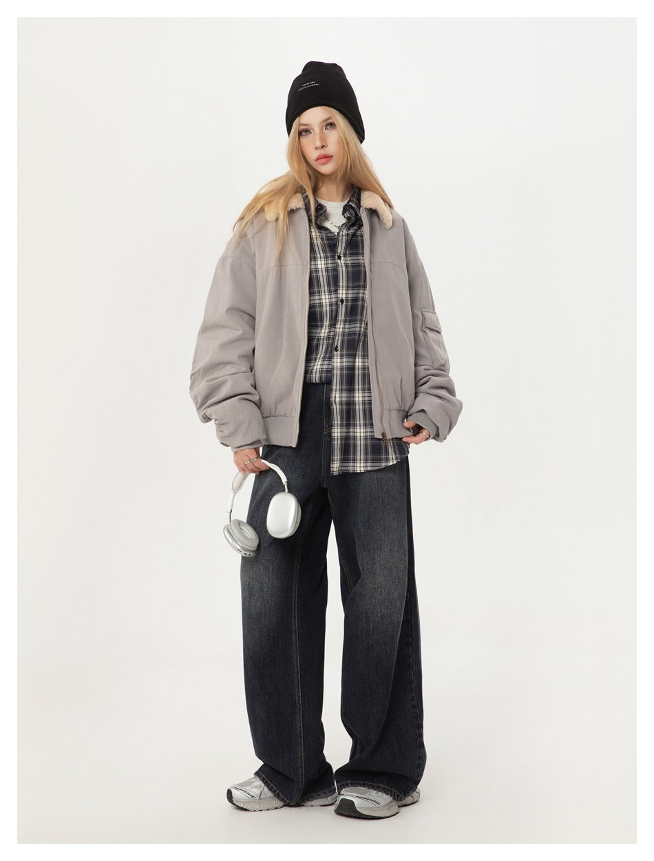 Model in light gray plush-collar bomber jacket worn open over a plaid shirt, with black beanie and dark jeans