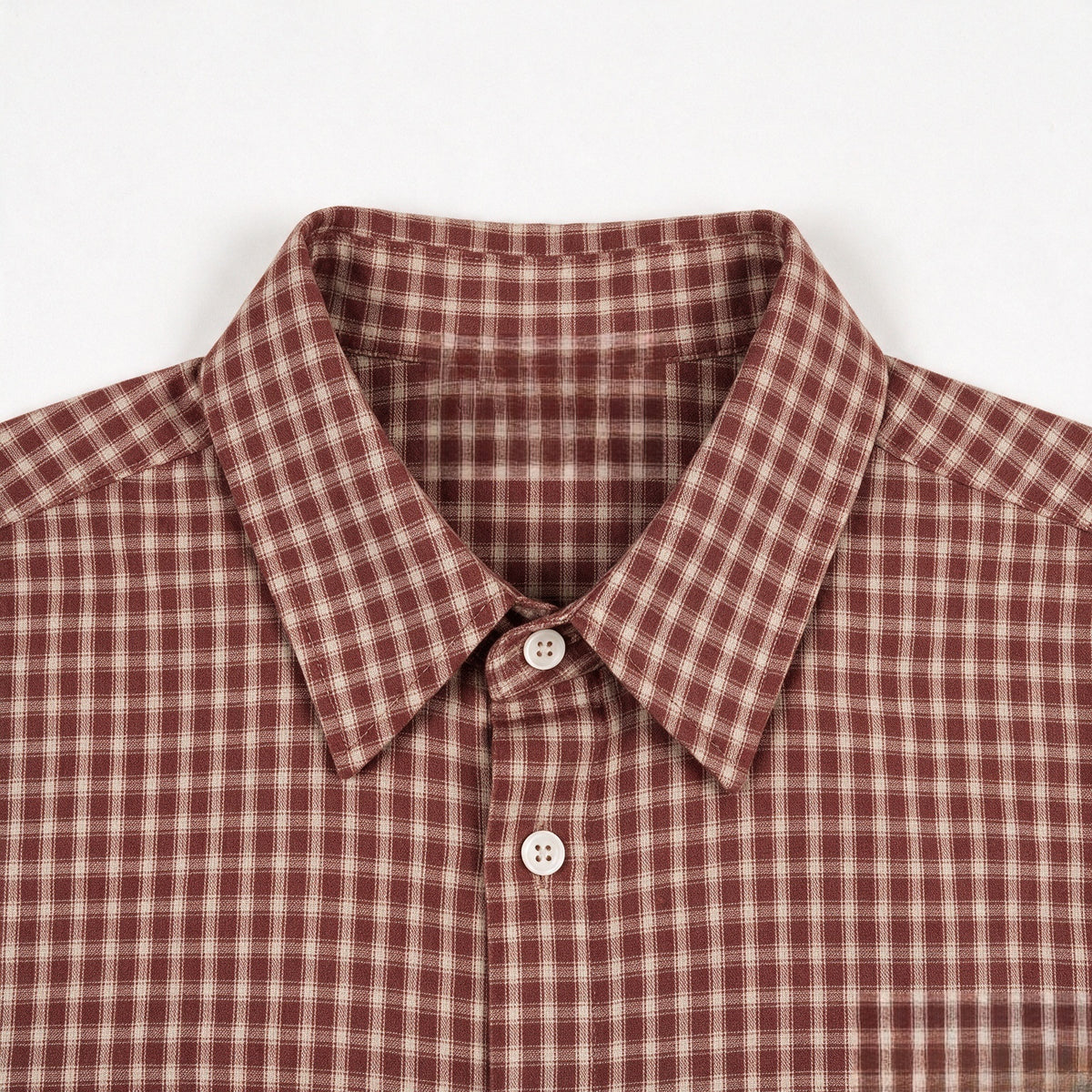 Close-up of a rust-red and cream plaid shirt collar, white buttons, and chest.