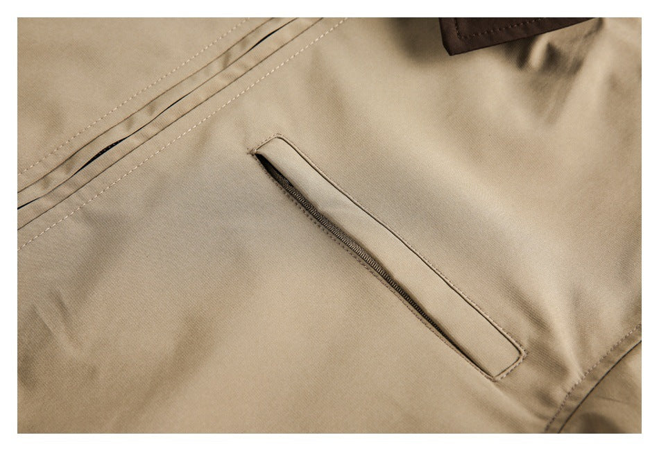 Close-up of a tan garment showing a narrow zip pocket, stitched seams, and part of a dark brown collar.